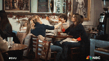 a group of people sitting at tables in a restaurant with the nbc logo on the bottom right