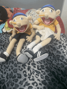 two stuffed dolls are sitting on a bed with a leopard print blanket