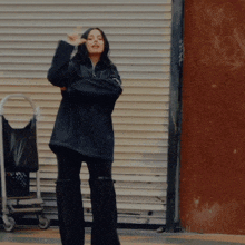 a woman in a black jacket and black pants stands in front of a garage door