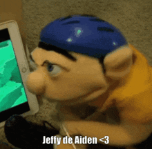 a puppet wearing a blue helmet is sitting in front of a tablet that says jeffy de aiden < 3 on it