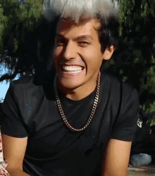 a man wearing a black shirt and gold chain smiles