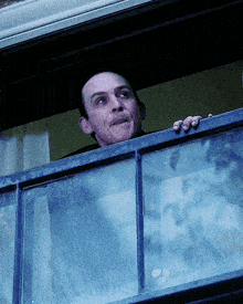 a man looks out of a window with his hand on the window sill