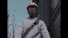 a man wearing a helmet and sunglasses holds a walkie talkie over his shoulder