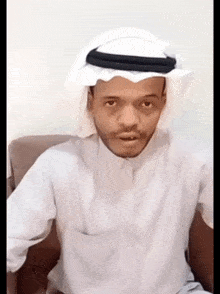 a man wearing a white shirt and a black head scarf looks at the camera