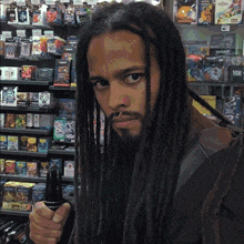a man with dreadlocks and a beard is holding a sword in front of a shelf of toys