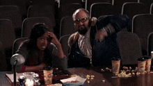 a man and a woman are sitting at a table with a tray of popcorn and a cup that says gourmet