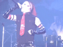 a man singing into a microphone on a stage with a drum set in the background