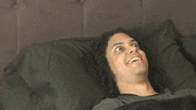 a man with curly hair is smiling while laying in bed with black pillows