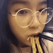a close up of a woman wearing glasses eating noodles with chopsticks .