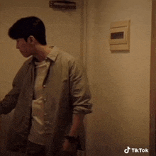 a man in a grey shirt is standing in a doorway next to a wall with a tiktok logo on it