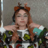 a woman wearing a grinch sweater and a reindeer headband holds her hair