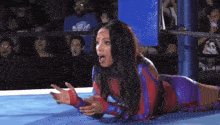 a woman in a wrestling ring is laying on the floor with her hands outstretched