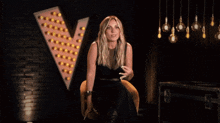 a woman in a black dress sits in front of a sign that says v