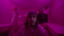a man with dreadlocks is standing in a room with purple lights and looking at the camera .