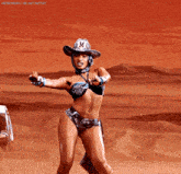 a woman in a bikini and hat is dancing in the desert .