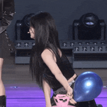 a woman in a black tank top is holding a blue balloon behind her back