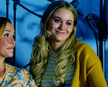 a woman wearing a yellow cardigan smiles next to another woman