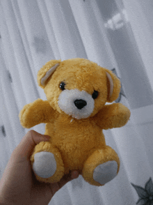 a yellow teddy bear is being held in someone 's hand