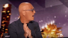 a bald man wearing glasses and a suit is sitting in front of a microphone on a stage .