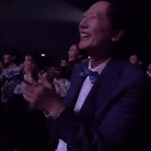 a man in a suit and bow tie is laughing while sitting in a crowd .