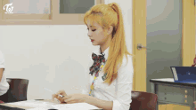 a girl with blonde hair is sitting at a desk in a classroom with a ponytail .