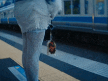 a woman standing on a train platform holding a stuffed animal in her hand