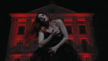 a woman in a black dress stands in front of a building with red lights