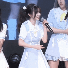 a girl in a light blue dress is holding a microphone and smiling