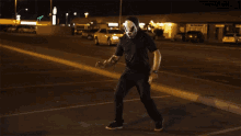 a man in a mask is holding a knife in a parking lot at night