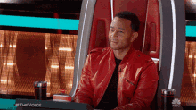 a man in a red leather jacket is sitting in a chair with a sign that says #thevoice