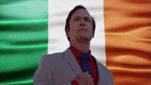 a man in a suit and tie stands in front of a irish flag
