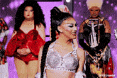 a group of drag queens are standing on a stage and one of them is wearing a braided top