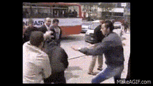 a group of men are fighting on a street in front of a bus that says nieasy on it .