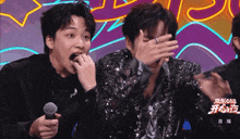 a man with a ring on his finger is covering his face while another man holds a microphone