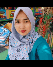 a woman wearing a hijab and a blue shirt is taking a picture of herself