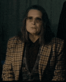 a woman wearing glasses and a plaid jacket looks serious
