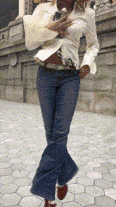a woman in a white shirt and blue jeans is walking down a sidewalk