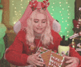 a woman in a red sweater is holding a gingerbread house .