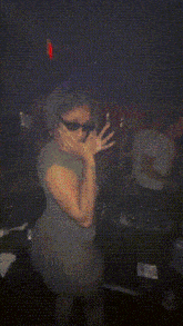 a woman wearing sunglasses and a gray dress is kneeling down in a dark room
