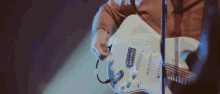 a person is playing a white electric guitar