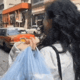 a woman is walking down the street holding a blue plastic bag