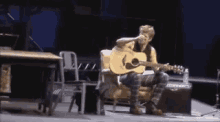 a man is sitting on a chair playing an acoustic guitar