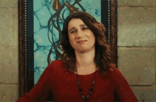 a woman in a red shirt is making a funny face in front of a framed picture .