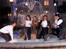 a group of people are standing in a fountain and one of them is kneeling down