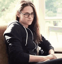 a woman wearing glasses and a black hoodie is sitting on a chair .