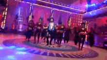 a group of people are dancing on a dance floor in a room with purple lights .