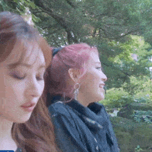 two women with pink hair are sitting next to each other in a park .