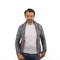 a man wearing a grey sweater and a white shirt stands with his hands in his pockets