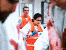 a woman in an orange vest is holding a bloody piece of meat