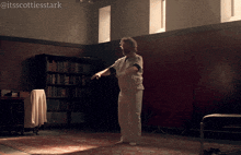 a man in a white shirt is standing in a dark room with a bookshelf in the background